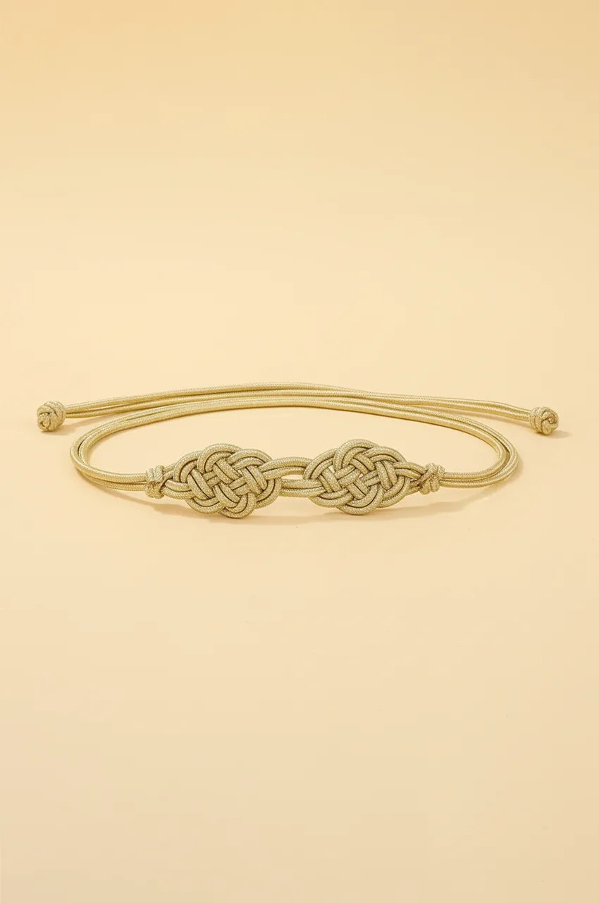 Front view of simple gold braided rope belt with knot details on beige background.