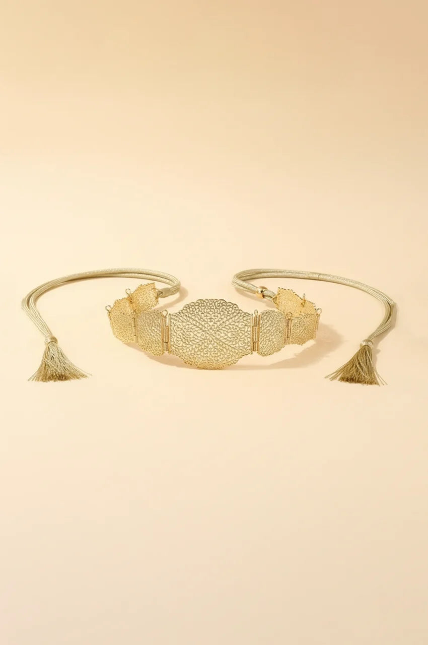 Flat lay of gold metal filigree belt with rope ties and tassels on beige background.