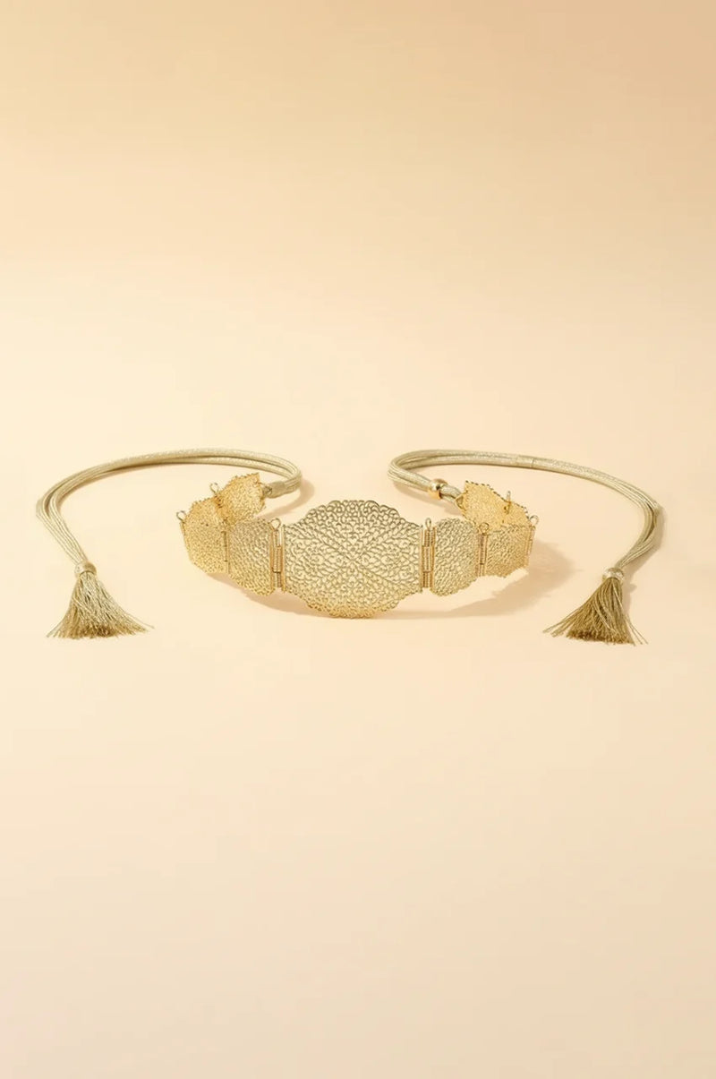 Flat lay of gold metal filigree belt with rope ties and tassels on beige background.