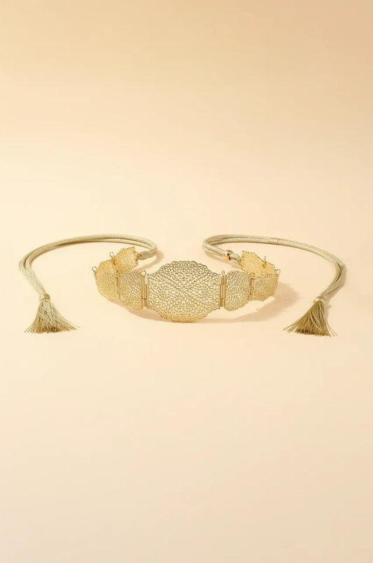 Flat lay of gold metal filigree belt with rope ties and tassels on beige background.