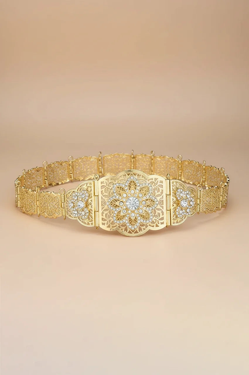 Full view of gold floral filigree belt with white crystal centerpiece on beige background.