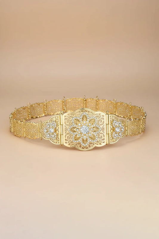 Full view of gold floral filigree belt with white crystal centerpiece on beige background.