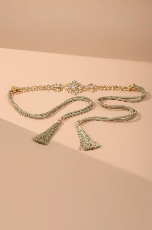 Full view of the Gold Geometric Rhinestone Spike Link Chain Belt with tassel ties on a beige background.