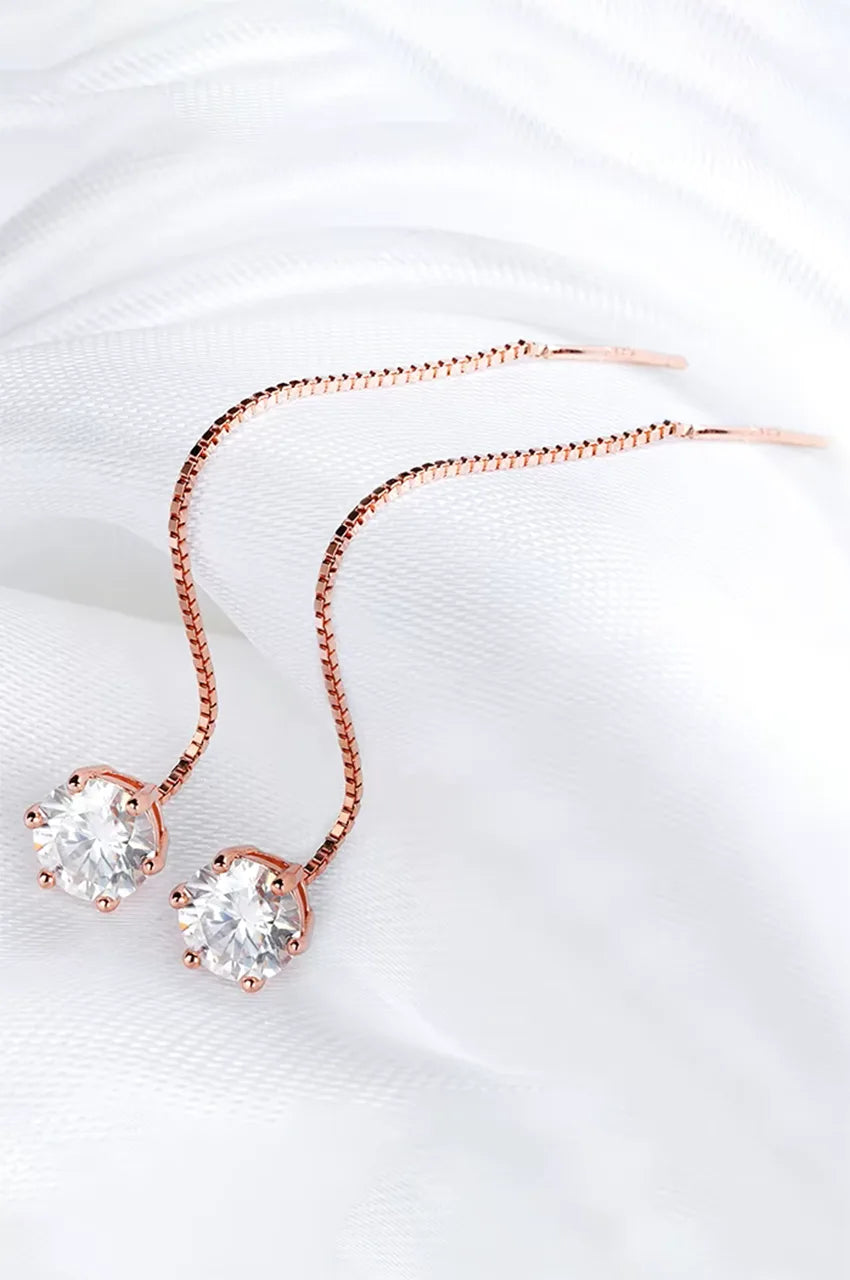 Elegant gold vermeil threader earrings with moissanite solitaires resting on soft white silk fabric.