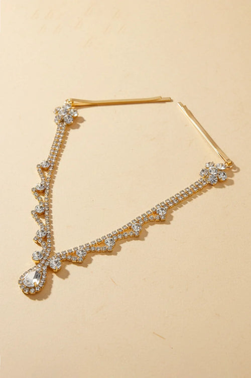 Full view of gold rhinestone forehead headpiece with teardrop crystal and hair pins on a beige background.