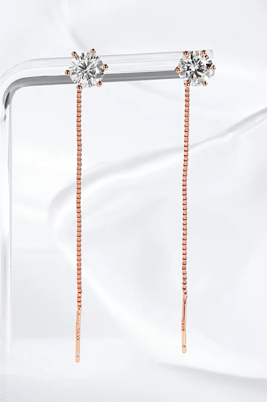 Gold tone box chain threader earrings with round brilliant moissanite stones hanging on a clear jewelry stand.
