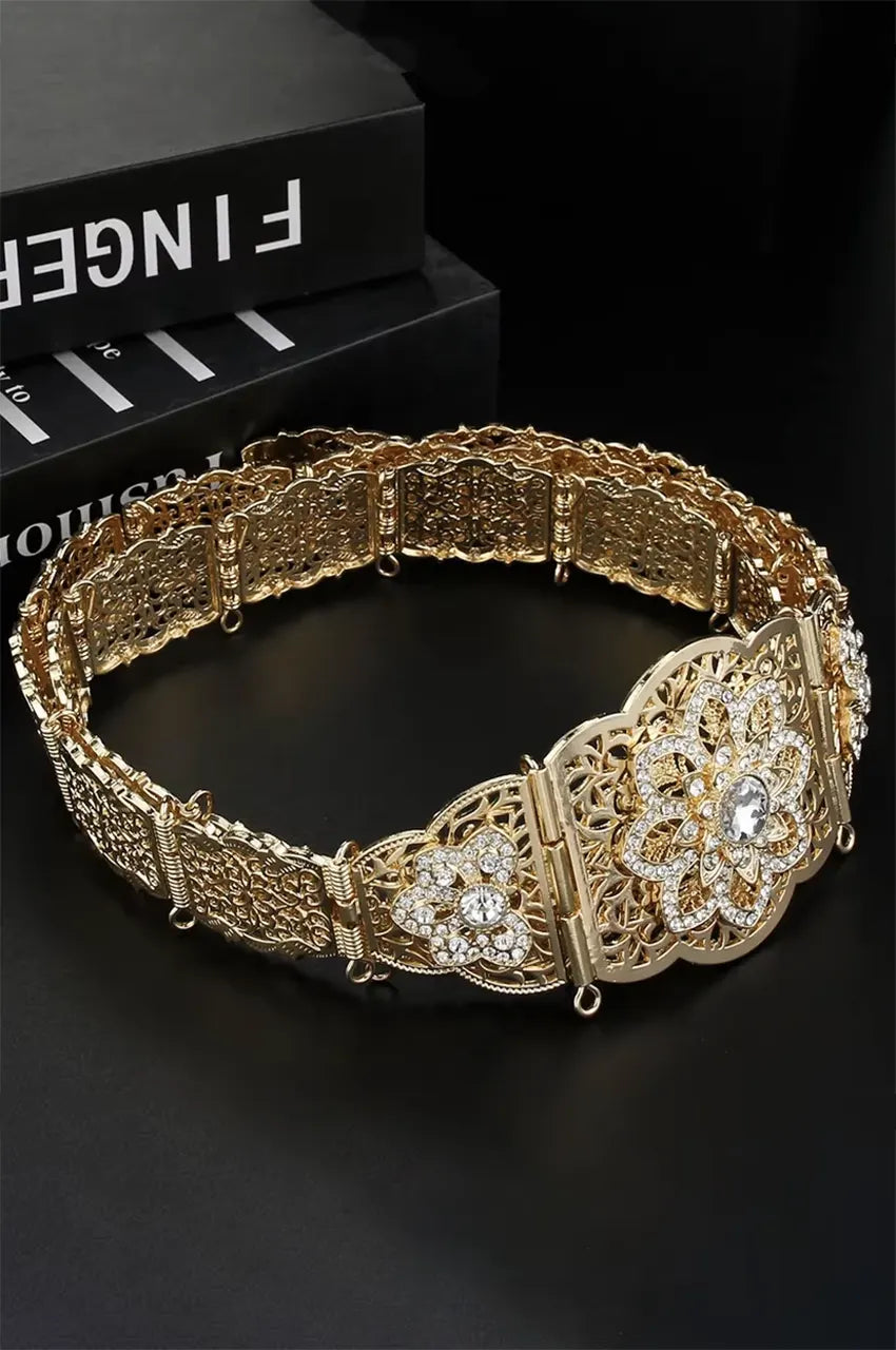 Side view of the gold metal belt showing the filigree plate details and white stones.