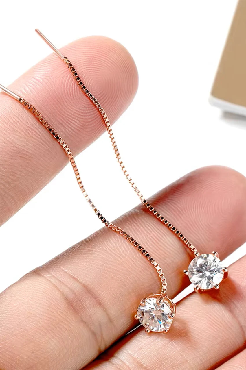 Close-up of hand holding long gold threader earrings demonstrating the chain length and stone sparkle.