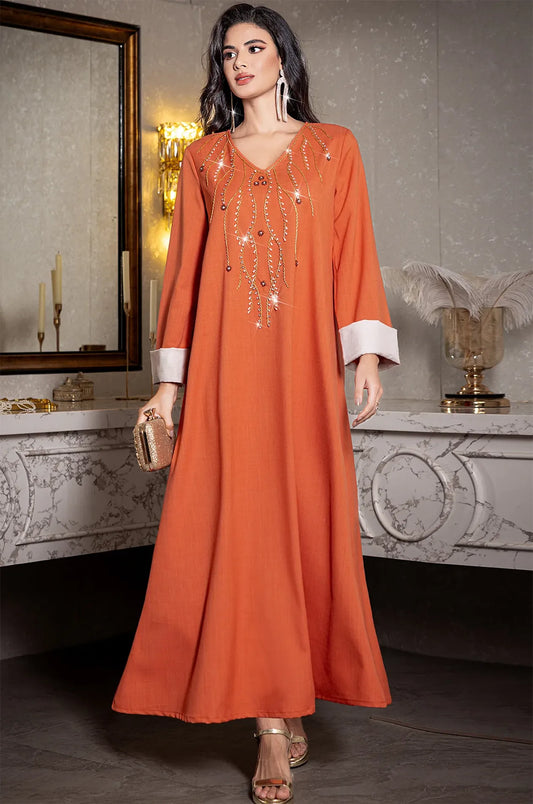 Model wearing the orange Ilena kaftan with a gold clutch in a luxury setting.