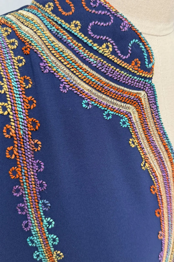 Extreme close-up macro shot of the high-quality braided embroidery on the navy blue fabric of the Inez Kaftan.
