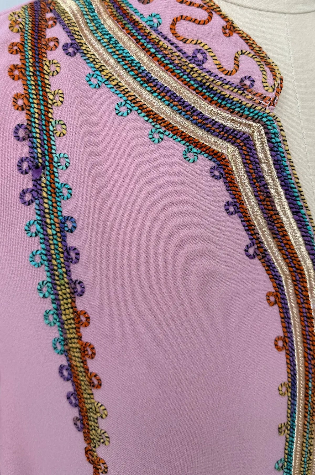 Macro texture shot of the multi-color braided embroidery on the dusty rose fabric of the Inez Jalabiya Kaftan.