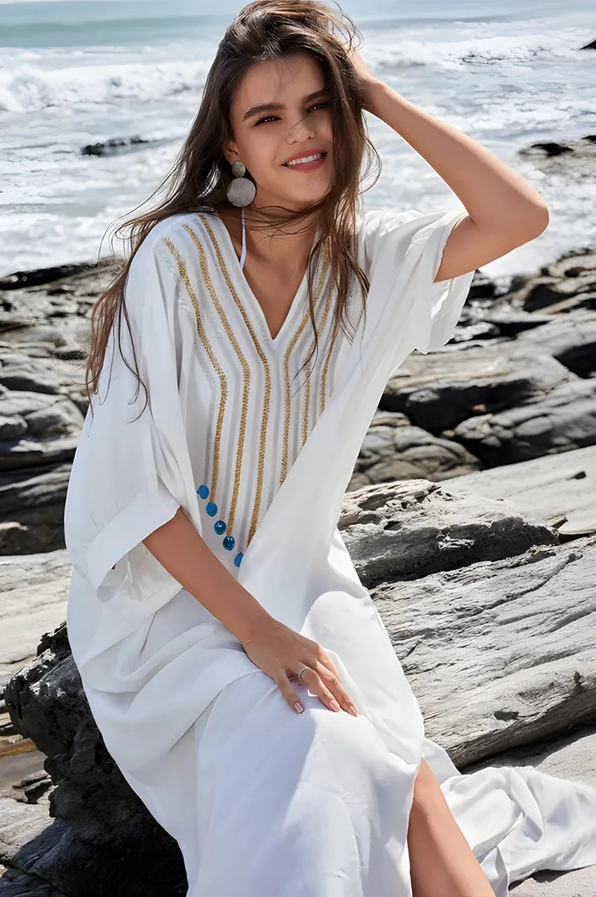 Woman sitting on rocks wearing Kalila white Greek kaftan with beaded design