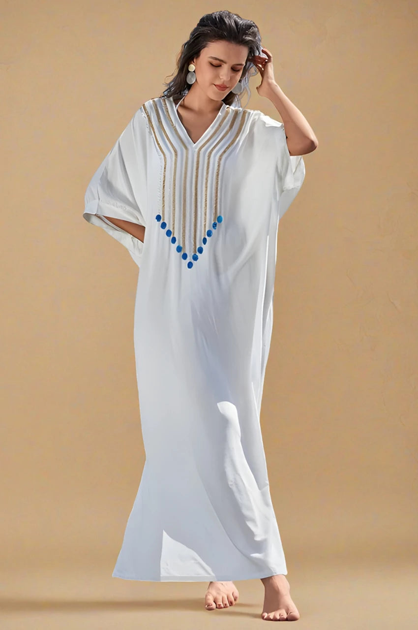 Model walking in Kalila white Greek kaftan with gold and blue bead detailing