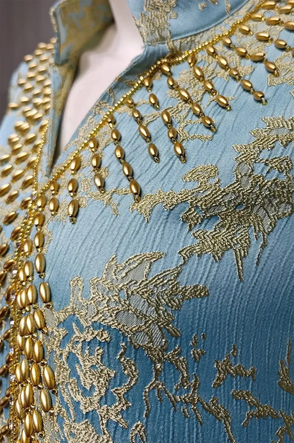 Macro close-up shot of the light blue textured jacquard fabric and hand-applied gold teardrop beads on the Estel kaftan.