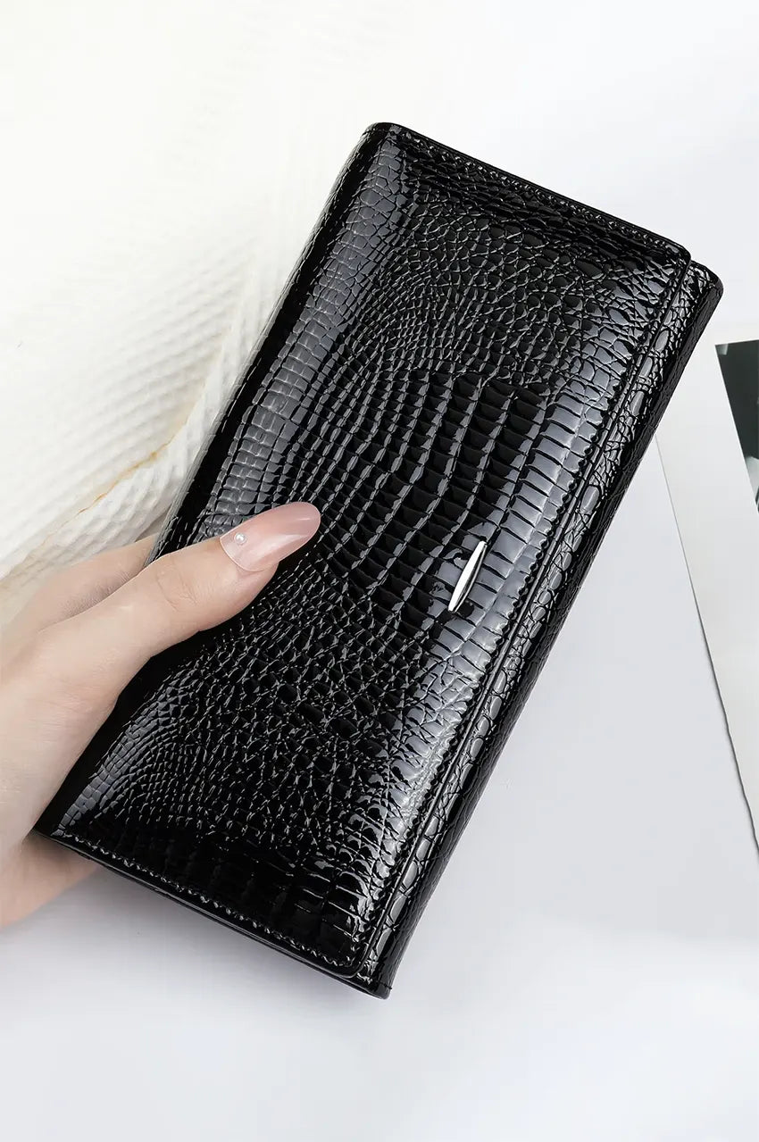 Woman's hand holding the sleek black patent leather wallet clutch, highlighting the glossy crocodile texture.