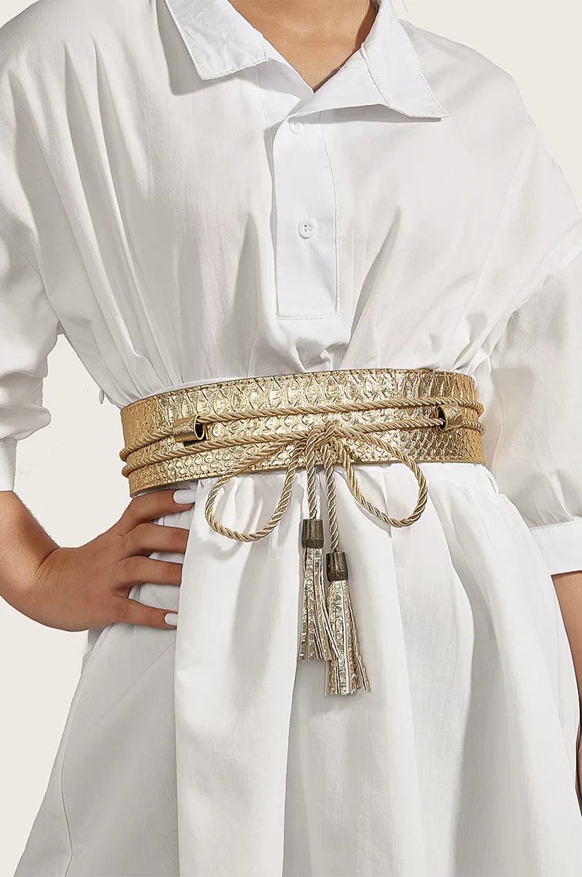 Woman wearing wide gold snake skin belt over a white tunic dress to cinch the waist.