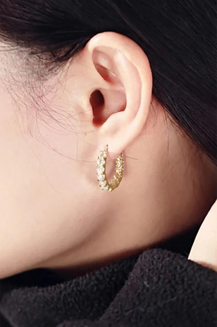 Side profile of a woman wearing gold paved huggie hoop earrings.