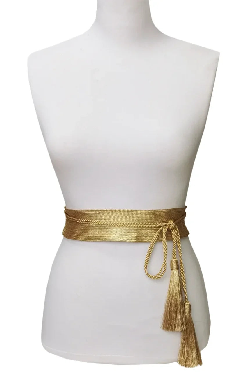 Woman wearing the wide gold sash belt over a white dress to define the waistline.
