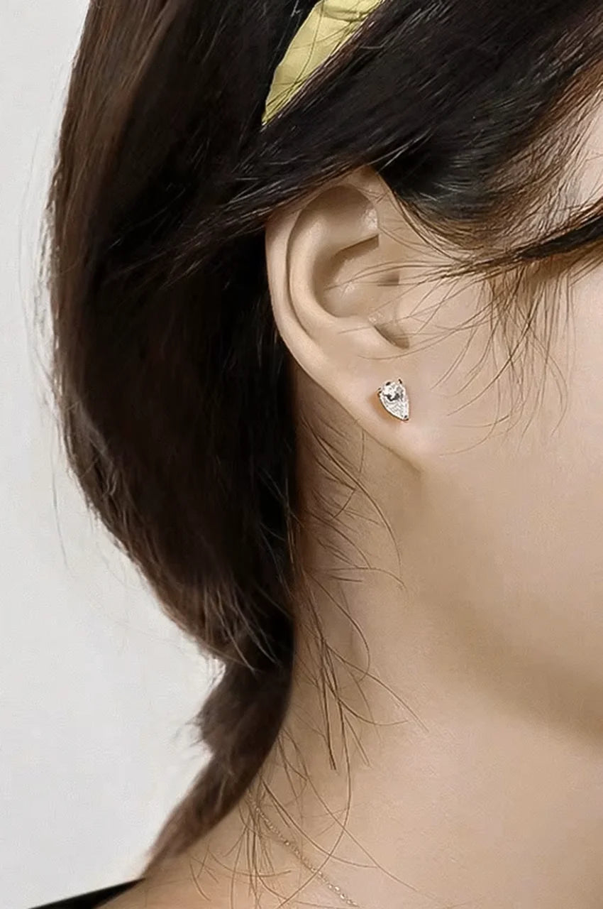 Close up of woman wearing a small silver pear-cut solitaire stud earring.