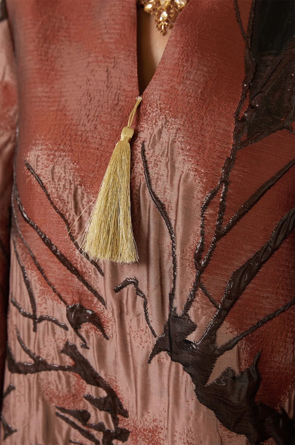 Close-up of the Naeli Red flowy kaftan featuring metallic rust fabric and a gold silk tassel at the neckline.