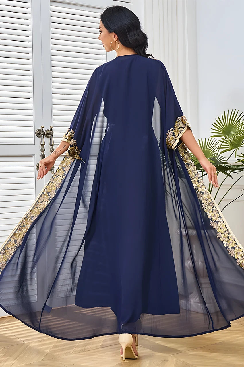 Movement shot of the navy blue and gold kaftan highlighting the fluid chiffon fabric and cape sleeves.