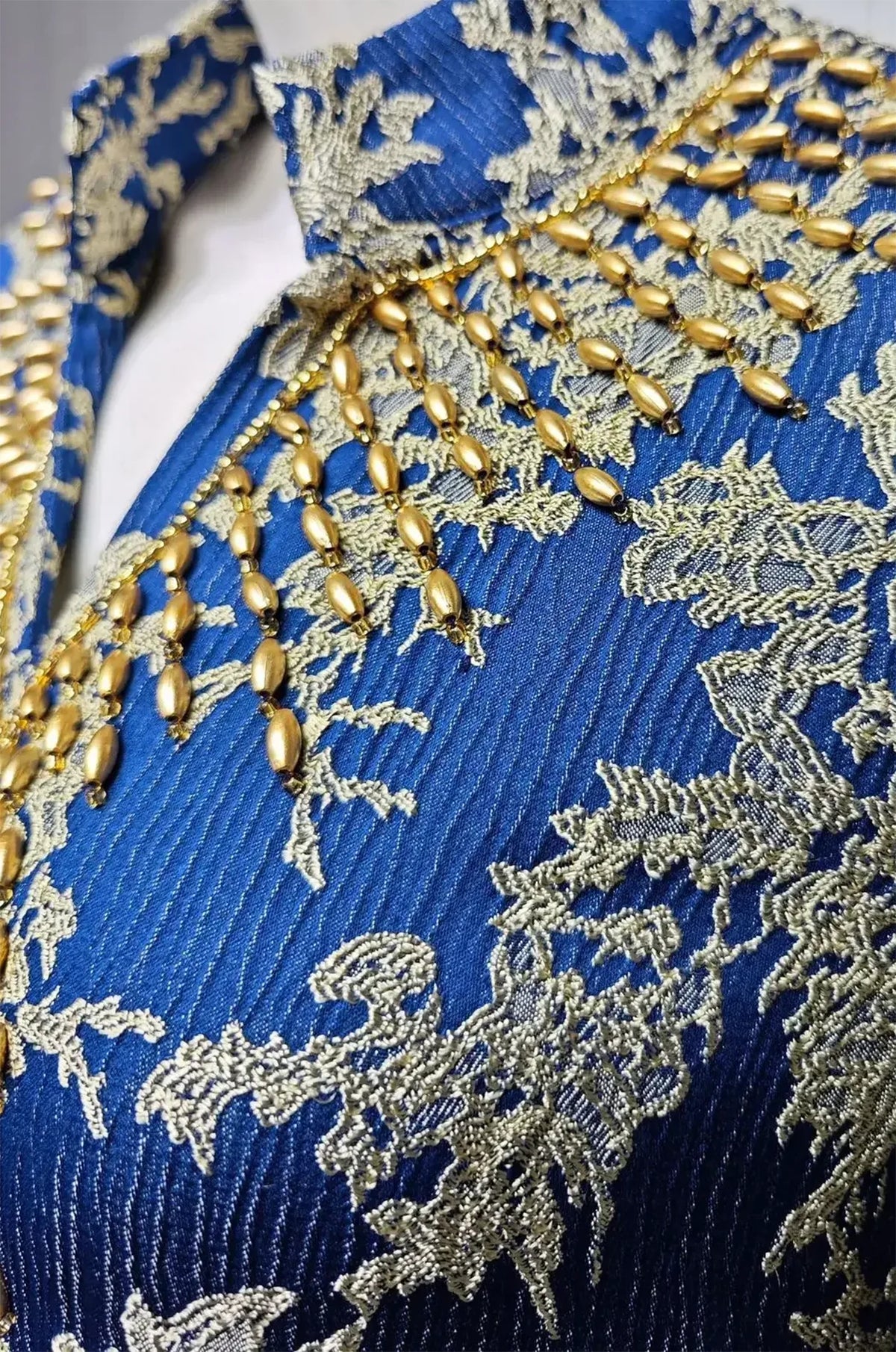 Extreme macro close-up of the navy blue jacquard texture, metallic gold floral threads, and hand-applied gold beads.