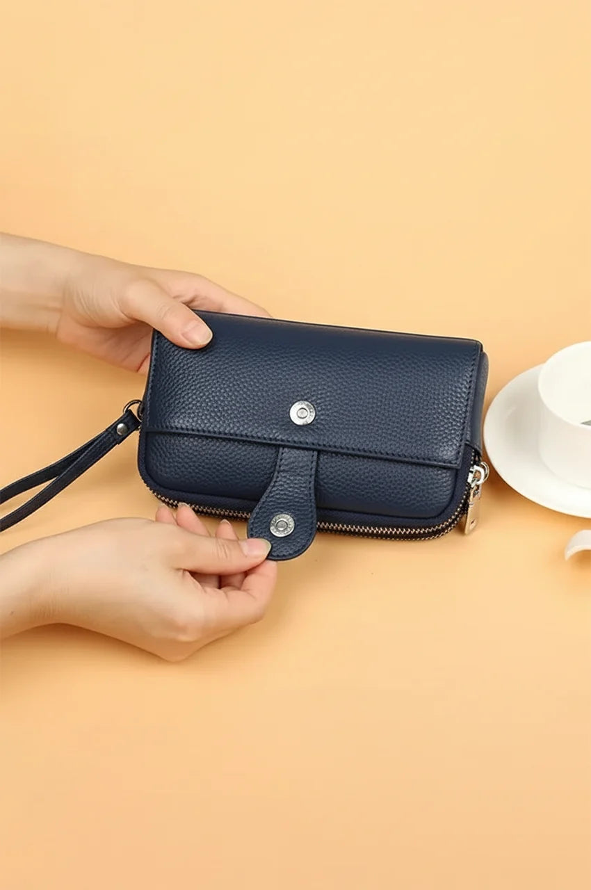 Hands opening the magnetic snap button on the front pocket of the navy blue leather clutch.