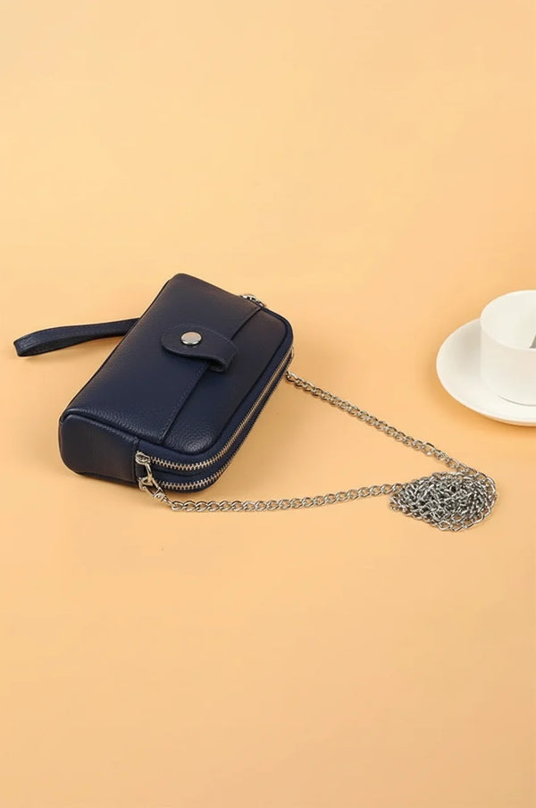 Angled side view of navy blue leather wristlet wallet showing pebbled texture and detachable chain.