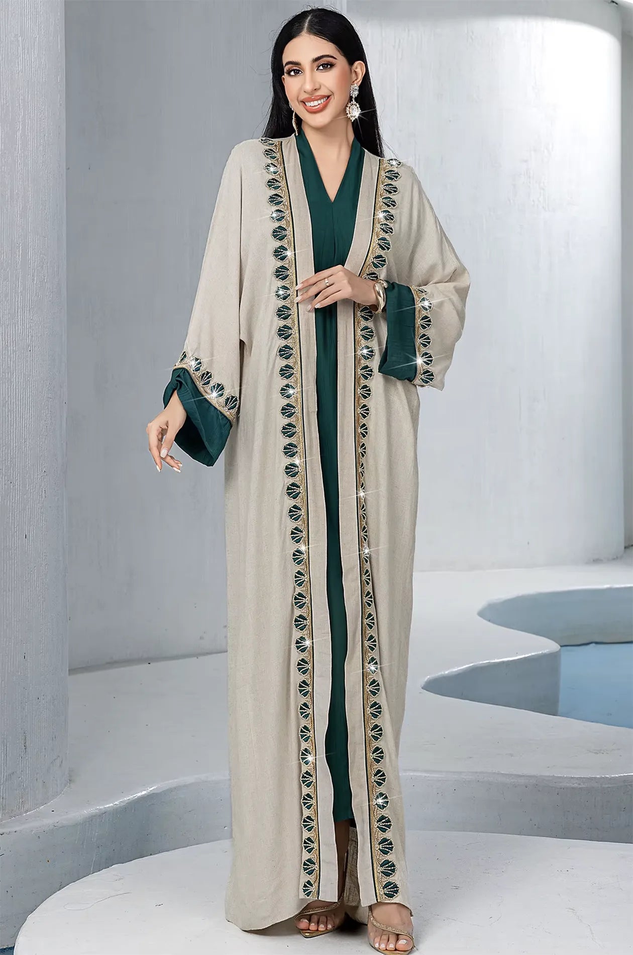 A smiling model wearing the Ameline beige kaftan dress with sparkling rhinestone details in a bright, modern lifestyle setting.