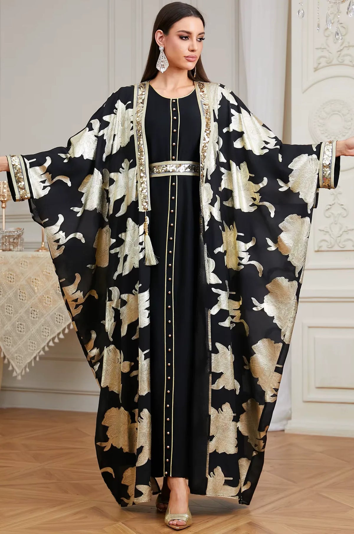 The Black Puppis kaftan luxe shown with arms extended to display the majestic cape wingspan and decorative gold tassel details.