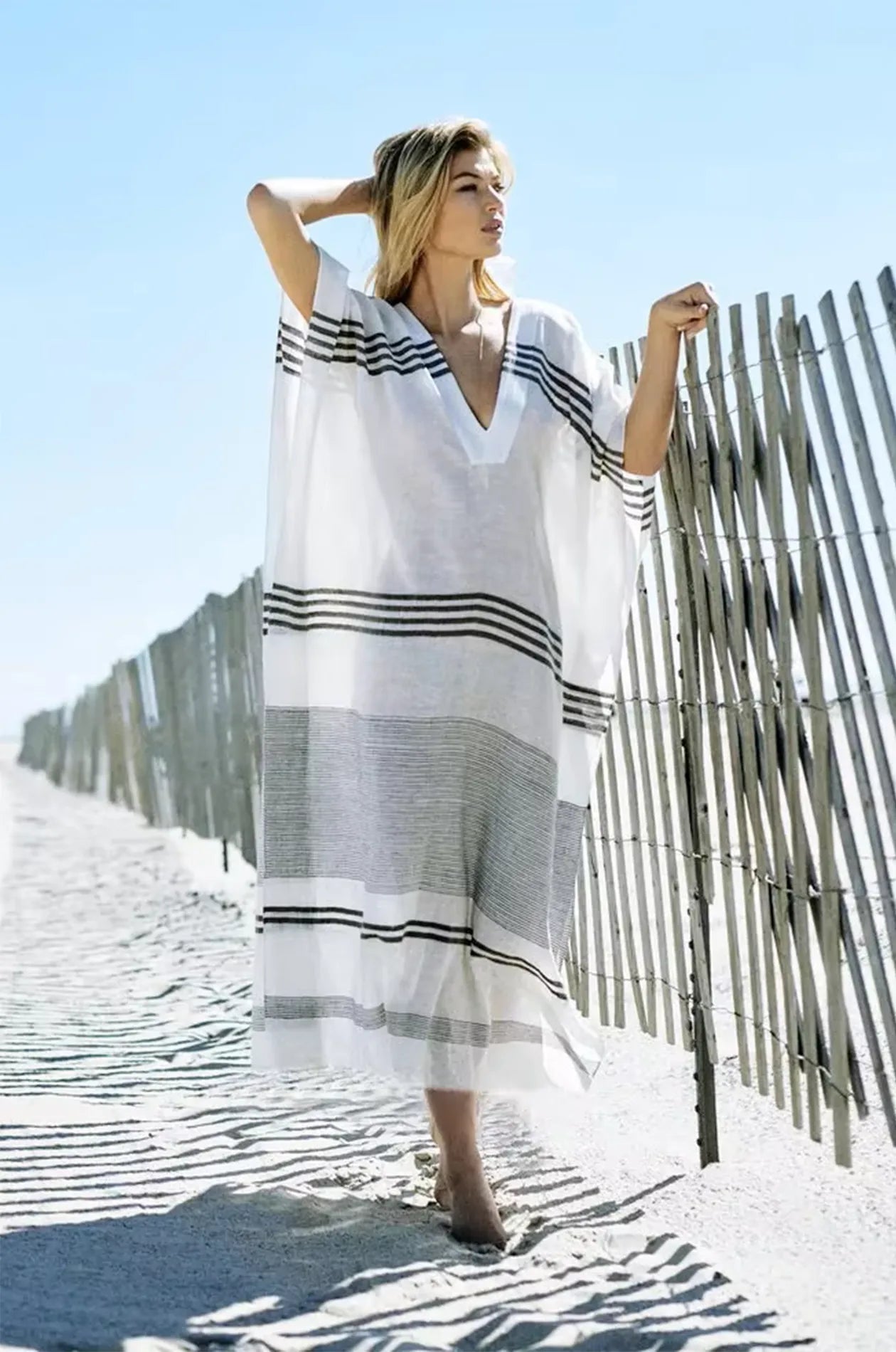 Naylara Dalia ivory white kaftan with bold charcoal stripes — beach lifestyle shot at wooden fence