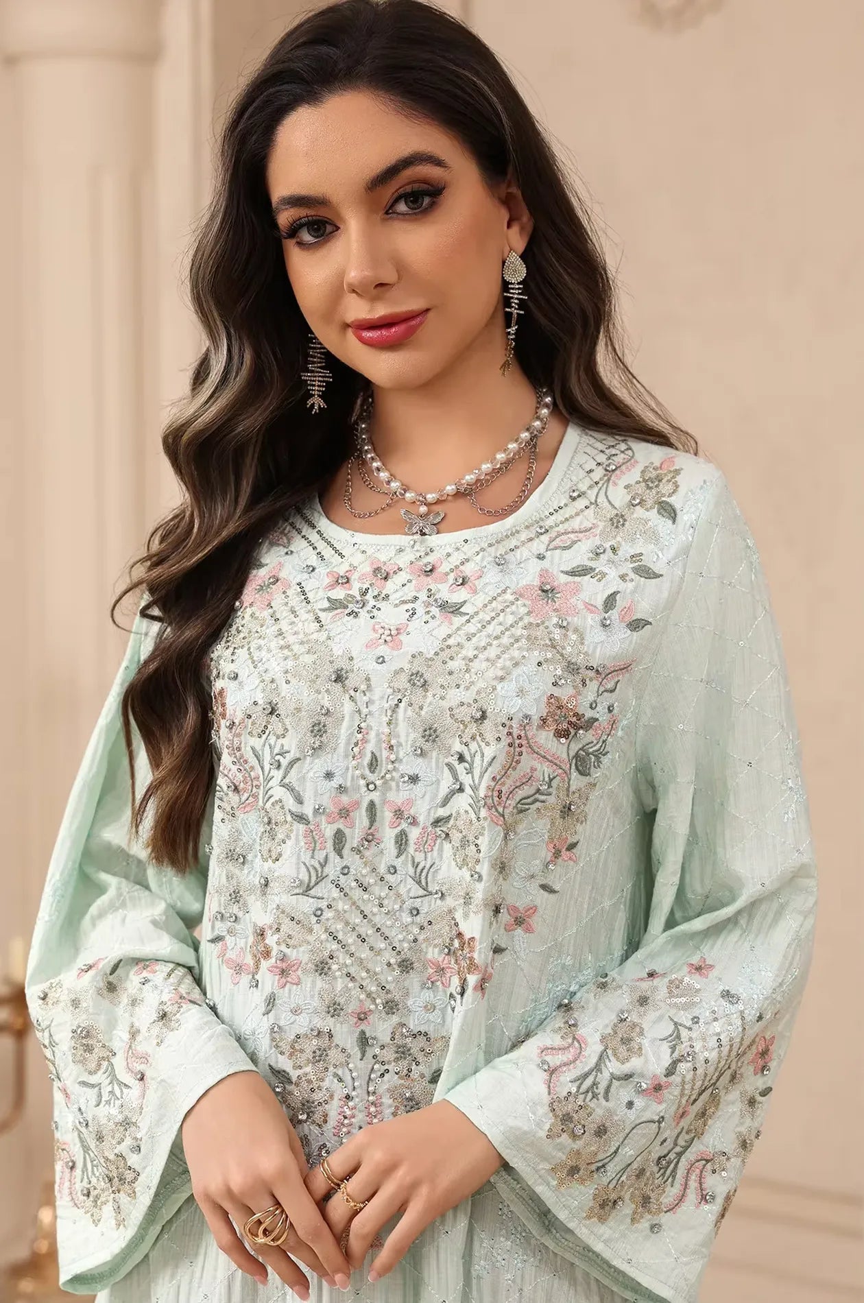 Detailed close-up of the multi-colored floral threadwork and sparkling beading on the green Equis modest kaftan.