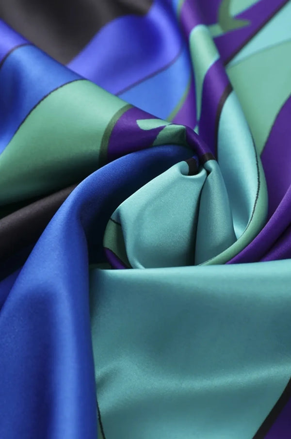 Macro detail of Naylara Erica satin fabric showing blue teal purple geometric print
