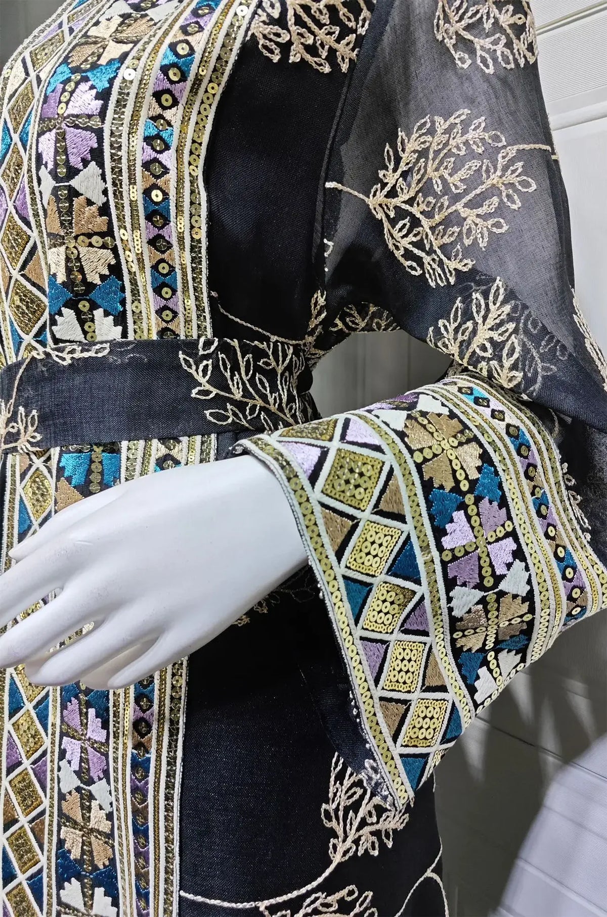 Extreme close-up of the hand-stitched beads and mosaic embroidery on the cuff of the Gienah black chic kaftan.