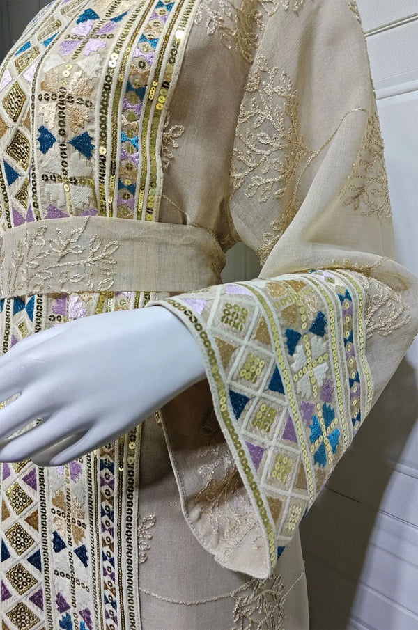 Macro detail of the hand-beaded sleeve cuff and gold sequins on the apricot beige Gienah chic kaftan on a mannequin.