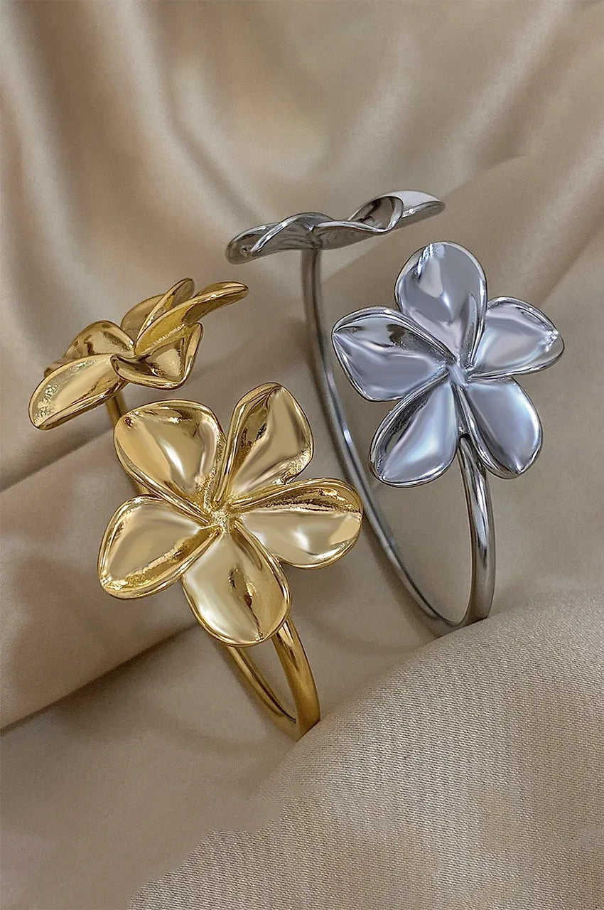 Comparison of gold and silver sculptural flower cuff bracelets on silk.