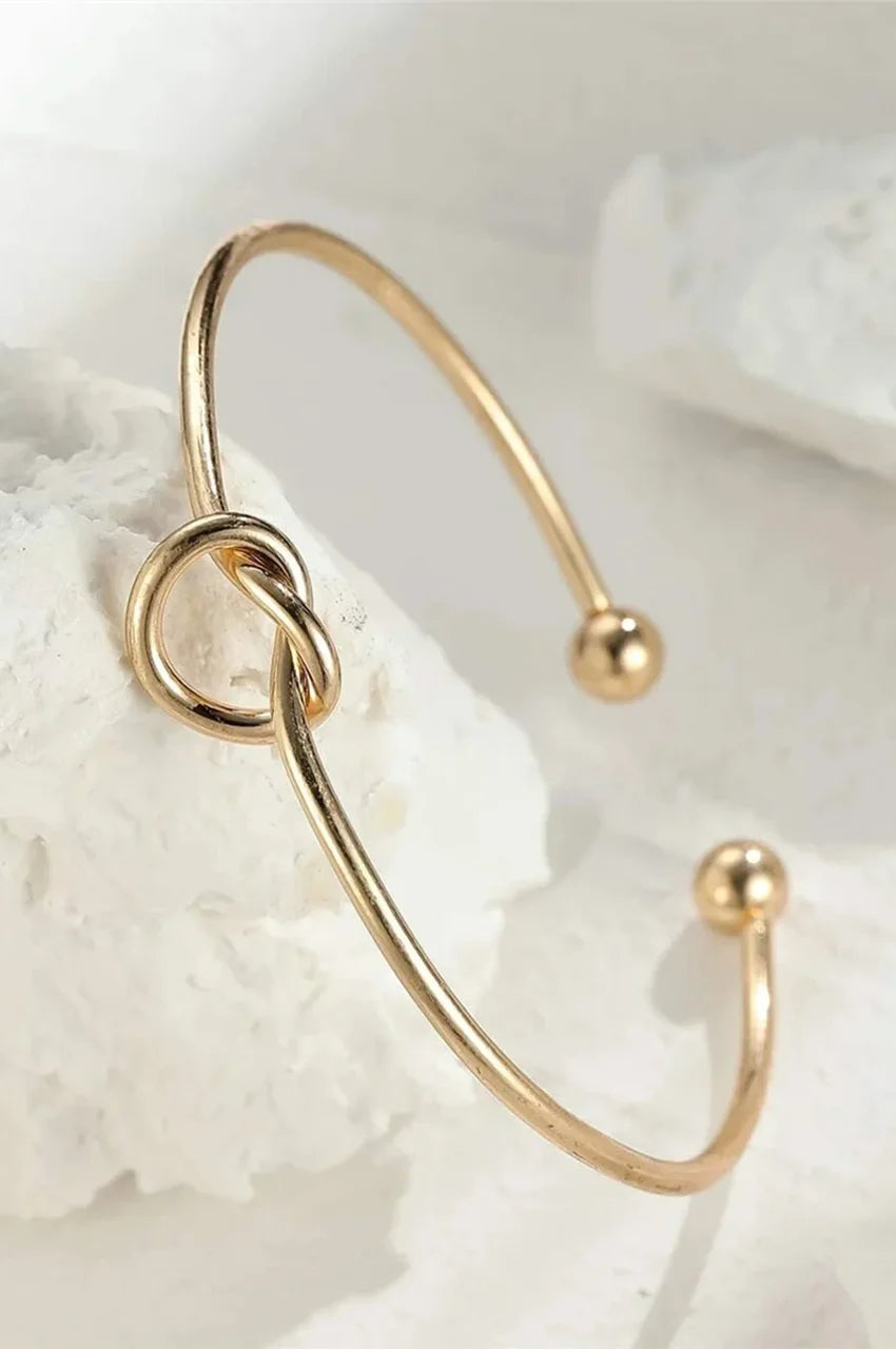 Artistic shot of gold knot bangle displayed on white textured stone.