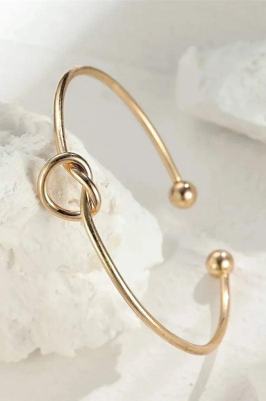 Artistic shot of gold knot bangle displayed on white textured stone.