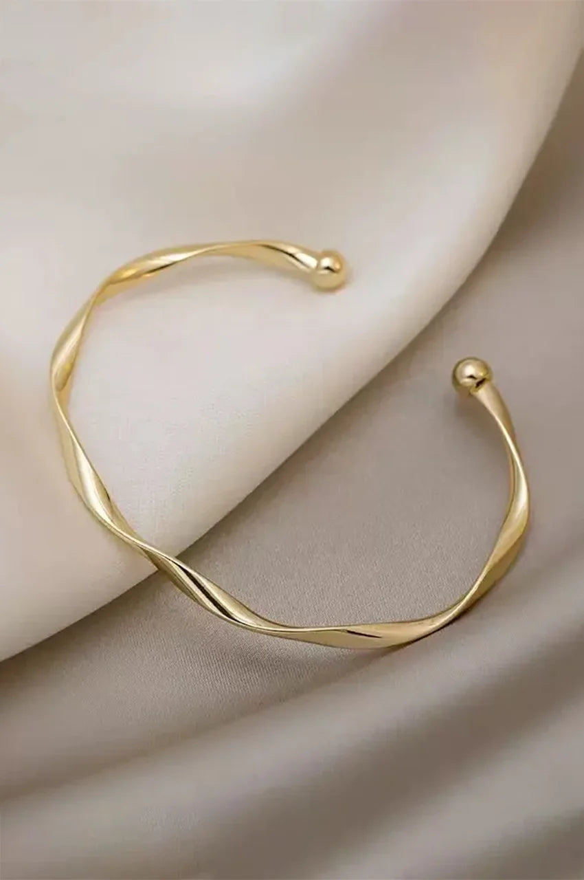 Gold twisted bangle bracelet displayed on soft silk fabric.