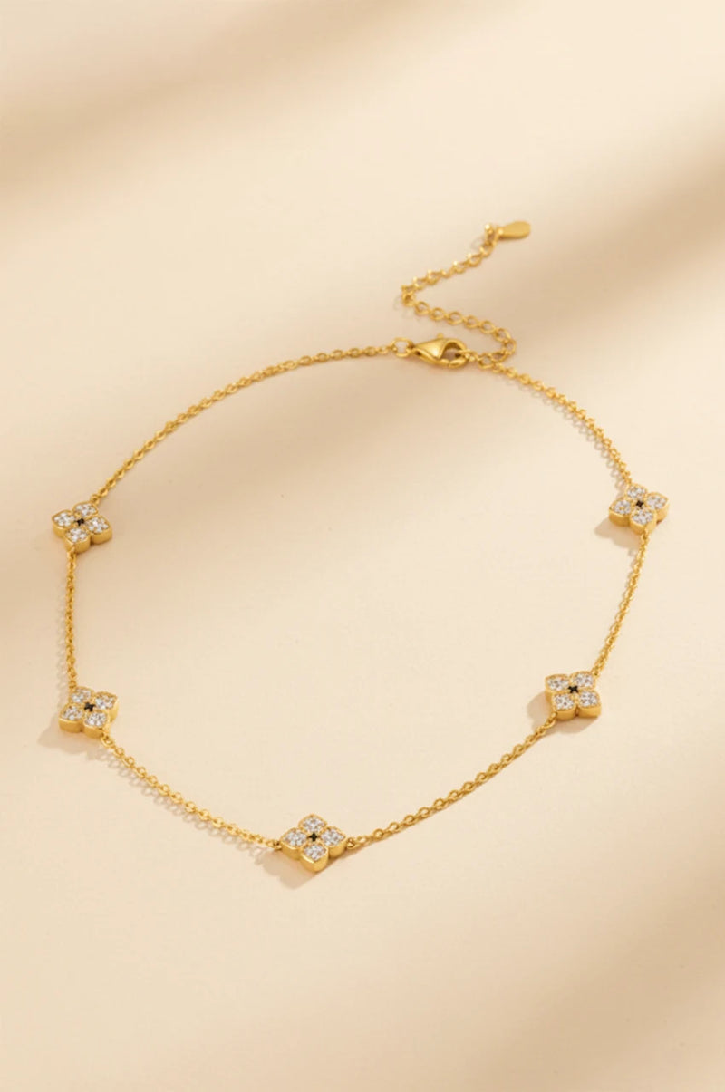Gold four-petal flower station necklace with moissanite flat lay on beige background