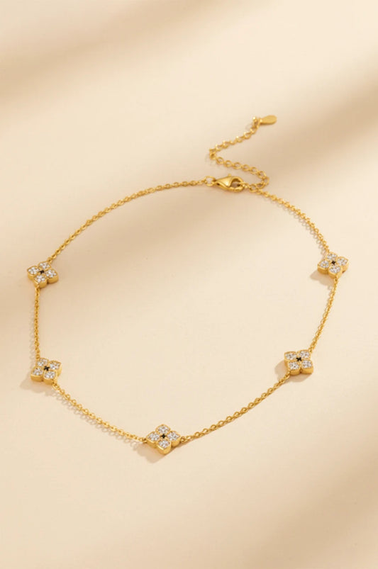 Gold four-petal flower station necklace with moissanite flat lay on beige background