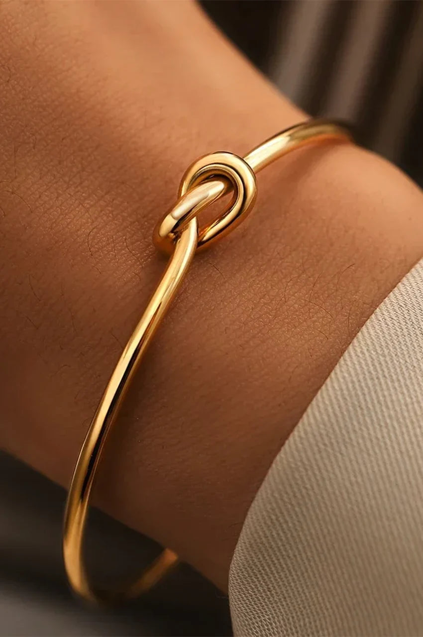 Close up of gold knot cuff bracelet worn on woman's wrist.