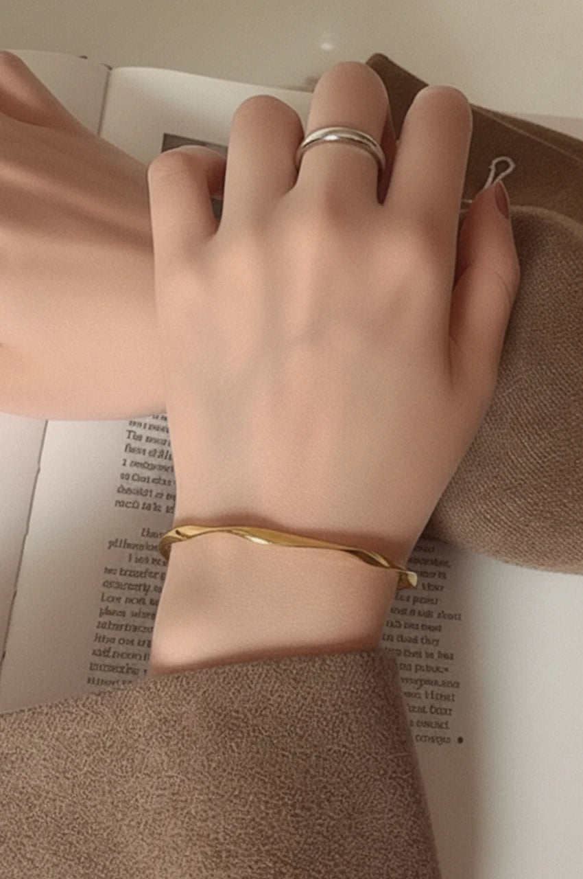 Woman wearing minimalist gold wave bangle on wrist.