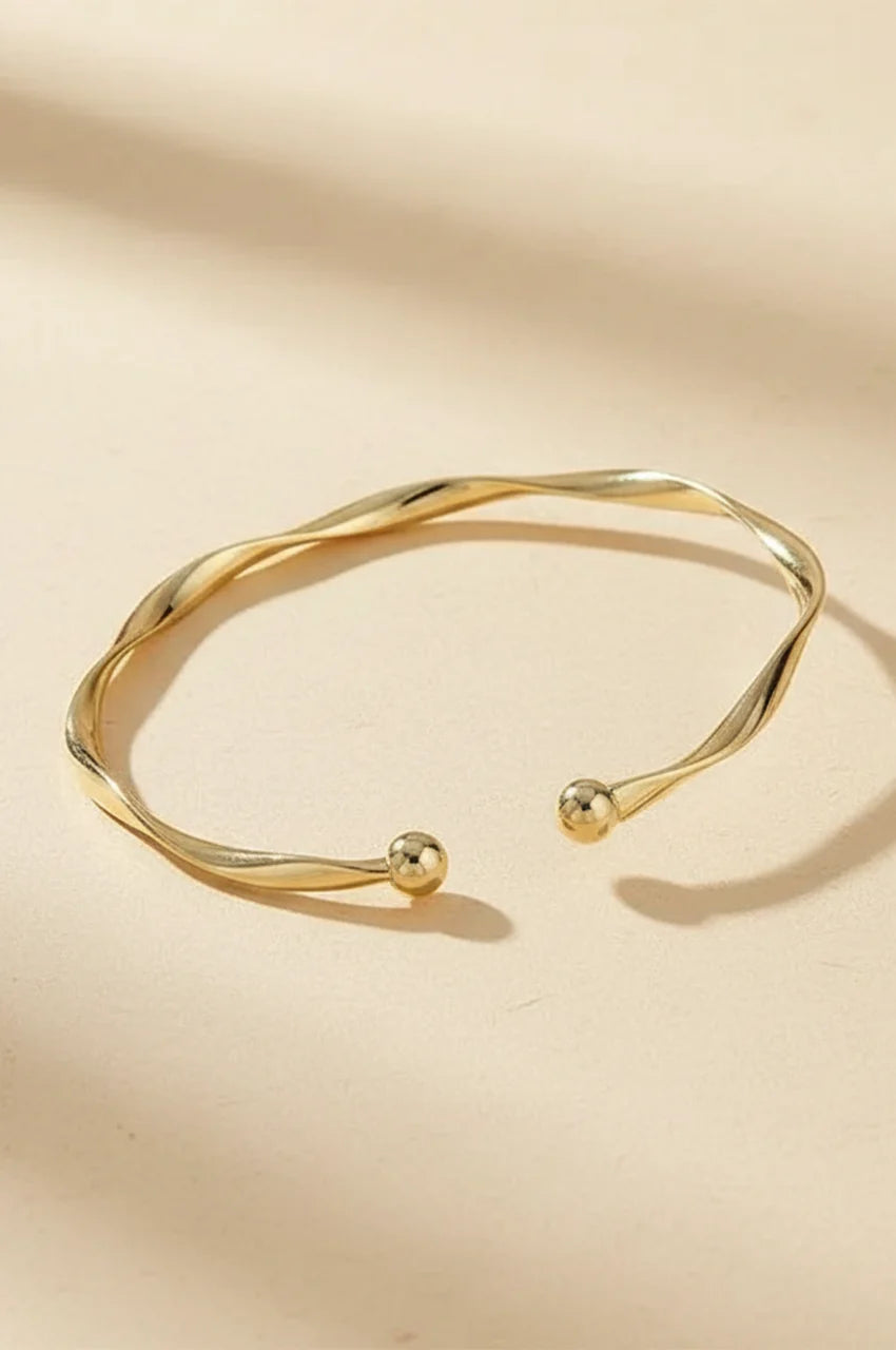 Minimalist gold twisted open cuff bracelet on beige background.