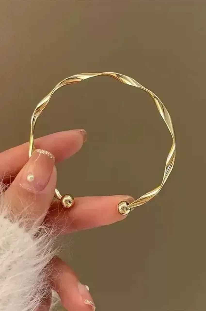 Close up of gold twisted bangle held in hand showing ball ends.