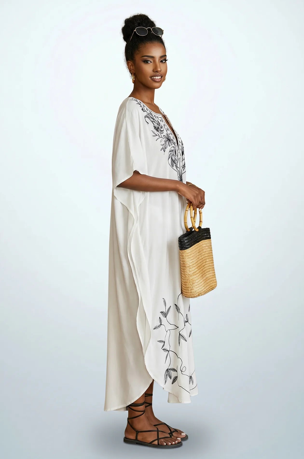Side profile of Naylara Halia white kaftan with black leaf embroidery and raffia tote bag