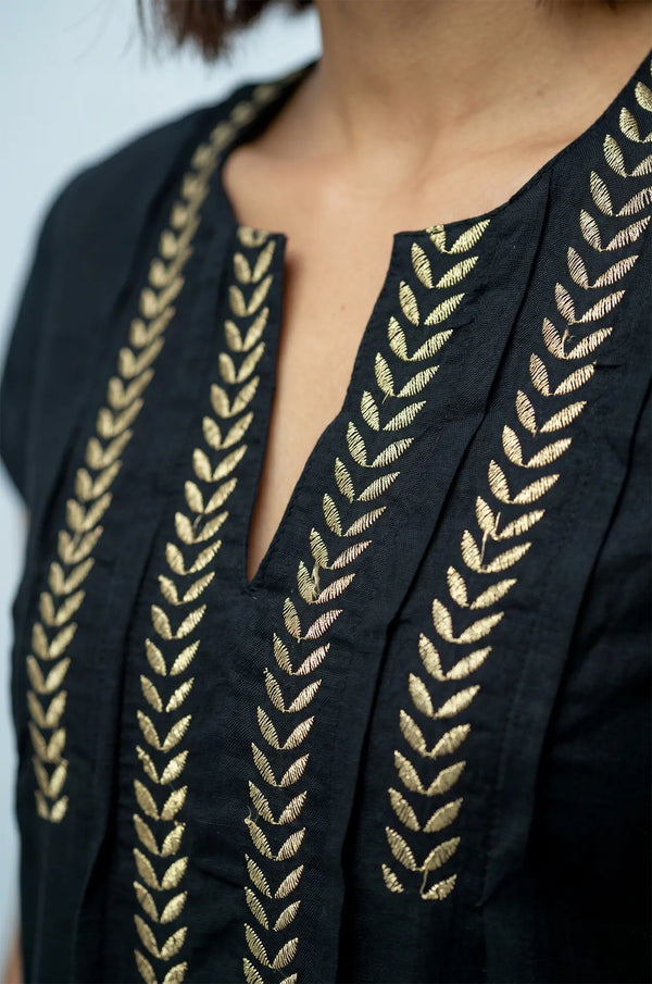 Macro detail of hand-embroidered gold wheat leaf motif on Naylara Iara black kaftan