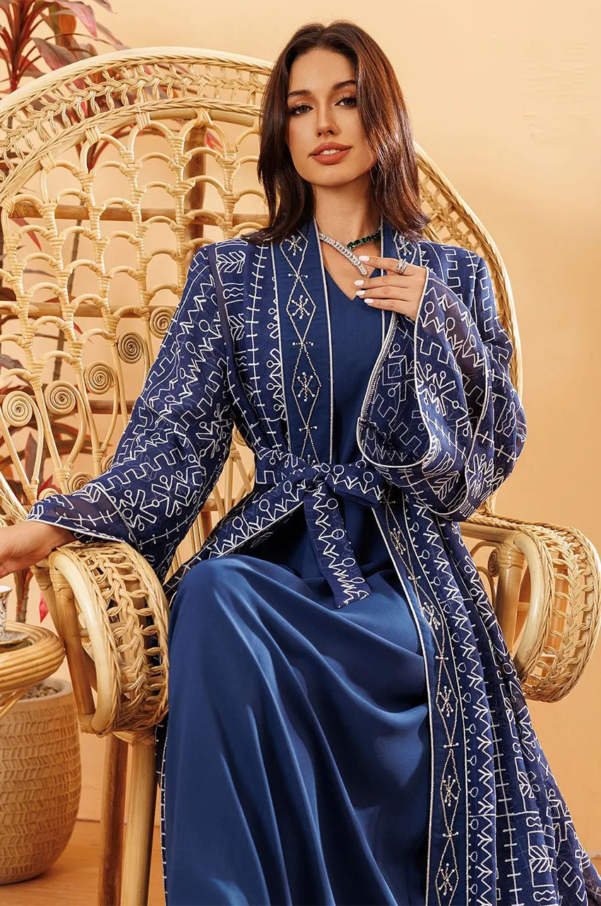 Model sitting wearing the Ilyah midnight blue embroidered belted kaftan dress styled for a luxury resort evening.