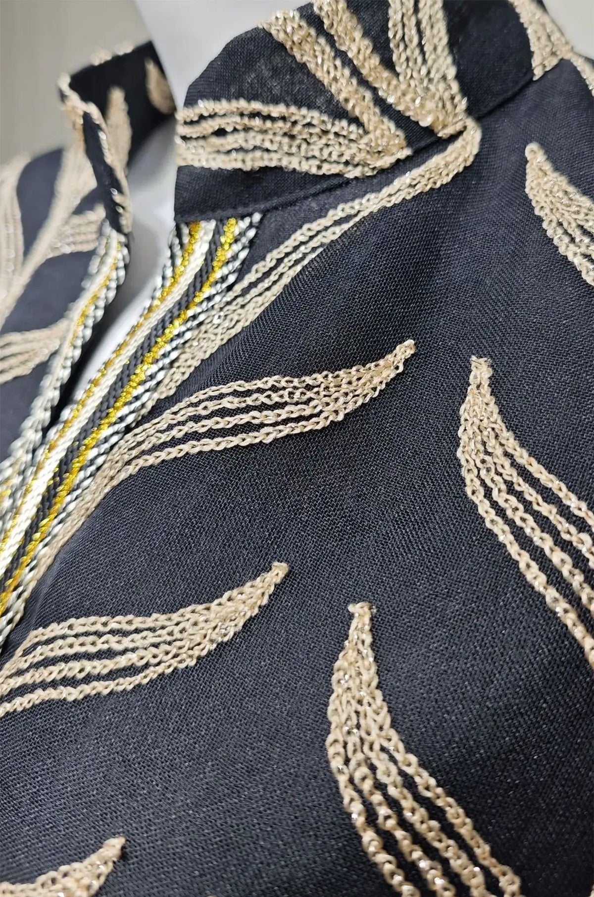 Macro close-up of the Kitala Kaftan's black sheer material, featuring high-quality metallic gold thread leaf embroidery and braided central trim.