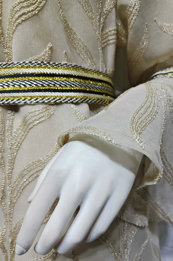 Close-up macro shot of the ivory beige Kitala Kaftan's embroidery, showing the high-quality metallic gold thread and detailed cuff finish.